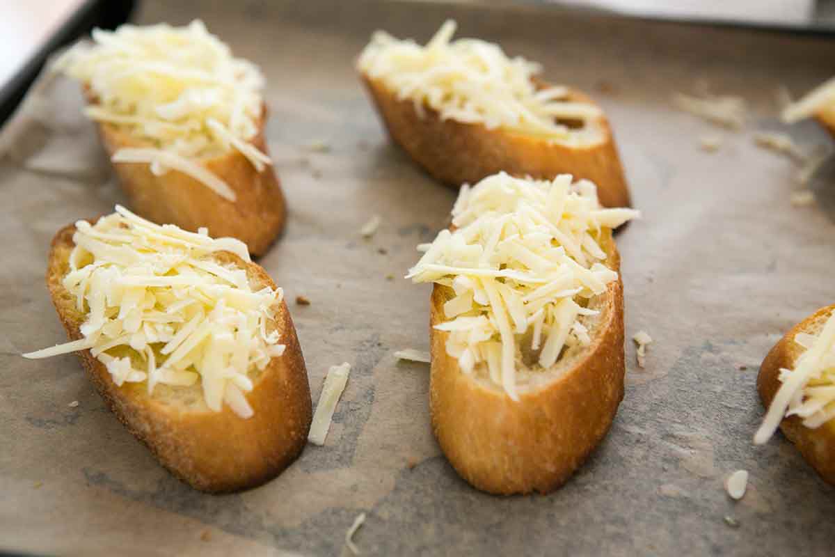 Shredded cheese placed on slices of French bread