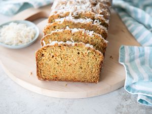 Slices of Zucchini Carrot Bread on Round Wood Board Next to Small Bowl of Coconut Flakes