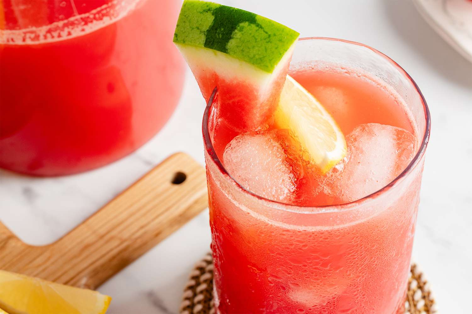 A glass of watermelemonade with ice garnished with a watermelon wedge and lemon slice