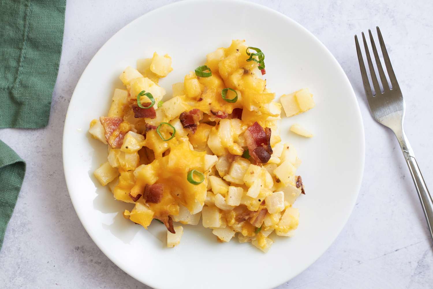 Plate of diced and cooked potatoes with melted cheese bacon and green onions