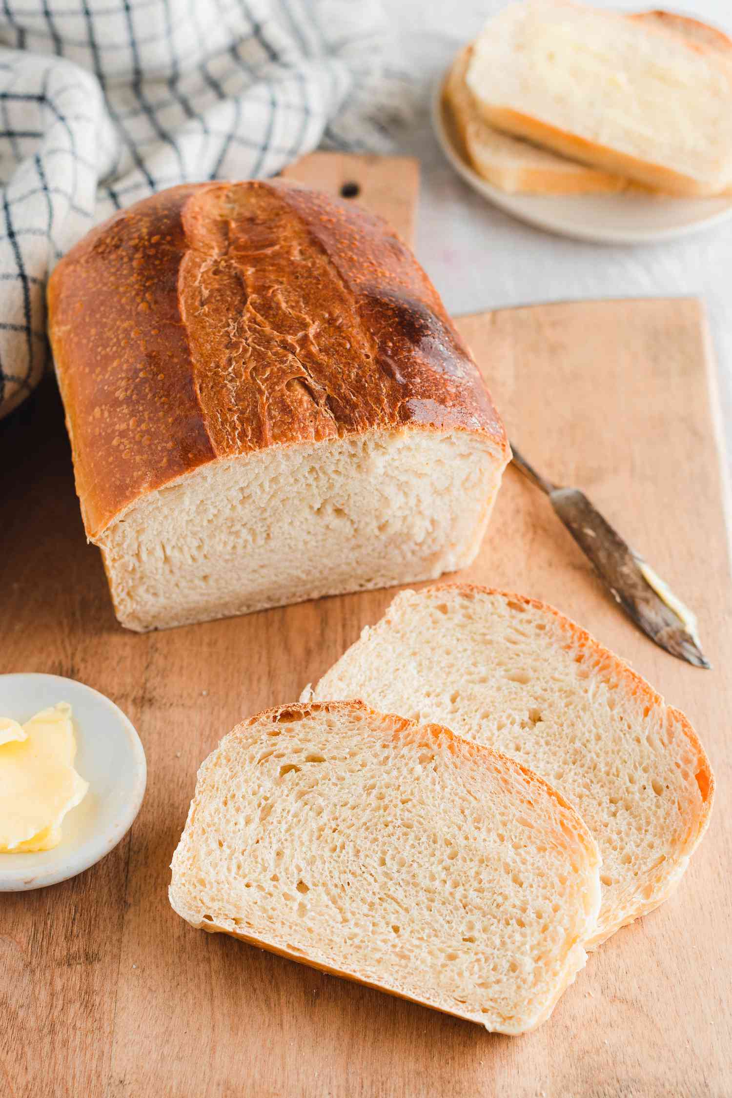 On a Cutting Board, a Sourdough Sandwich Loaf Next to Slices of Sourdough Loaf and a Small Saucer of Butter 