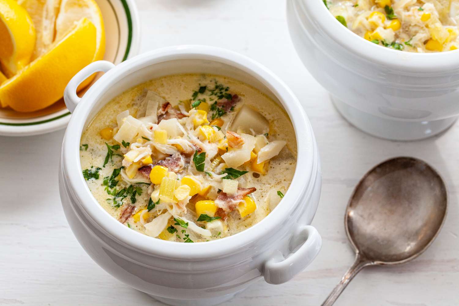 Corn and Crab Chowder in a Soup Bowl with Handles Next to Another Bowl of Chowder and a Bowl of Lemon Slices