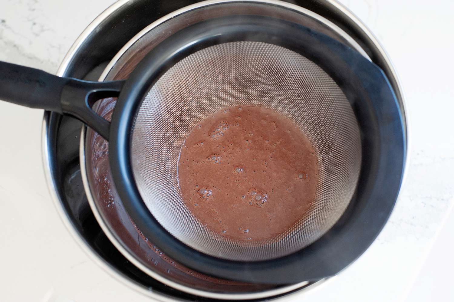 A strainer set over a bowl to show how to make chocolate ice cream.
