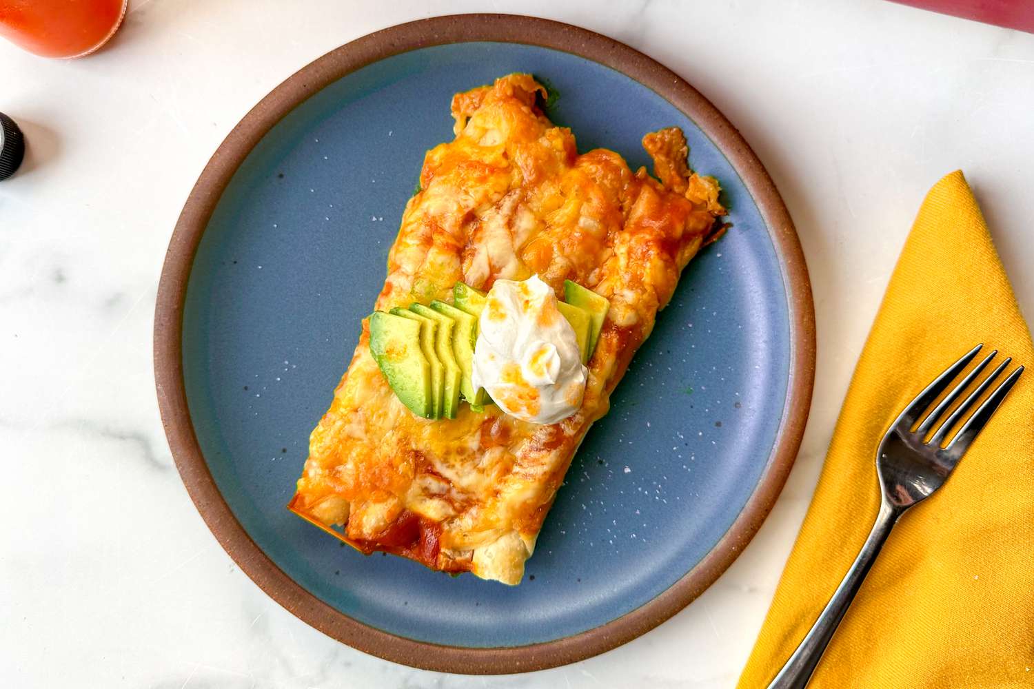 Taquito enchiladas on a blue plate topped with avocado and sour cream