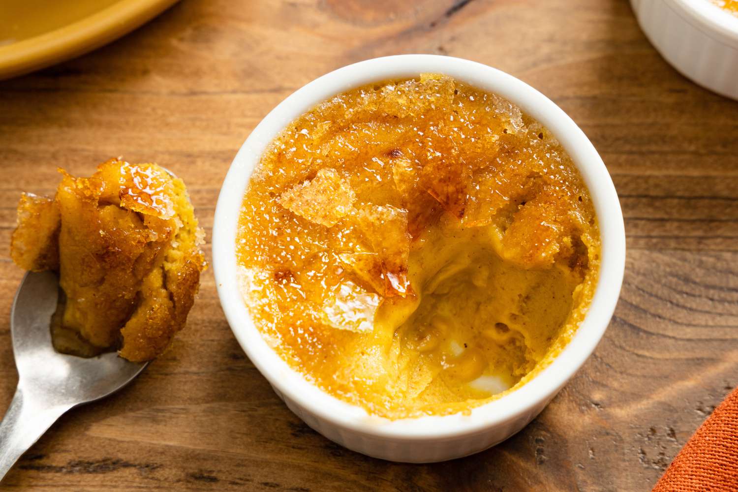 A 3-Ingredient Pumpkin Spice Crème Brûlée in a Ramekin, after Broken into with a Spoon. Spoon with Creme Brulee on It Next to Ramekin.