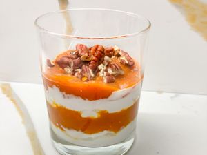 Layered yogurt and pumpkin dessert topped with pecans in a glass