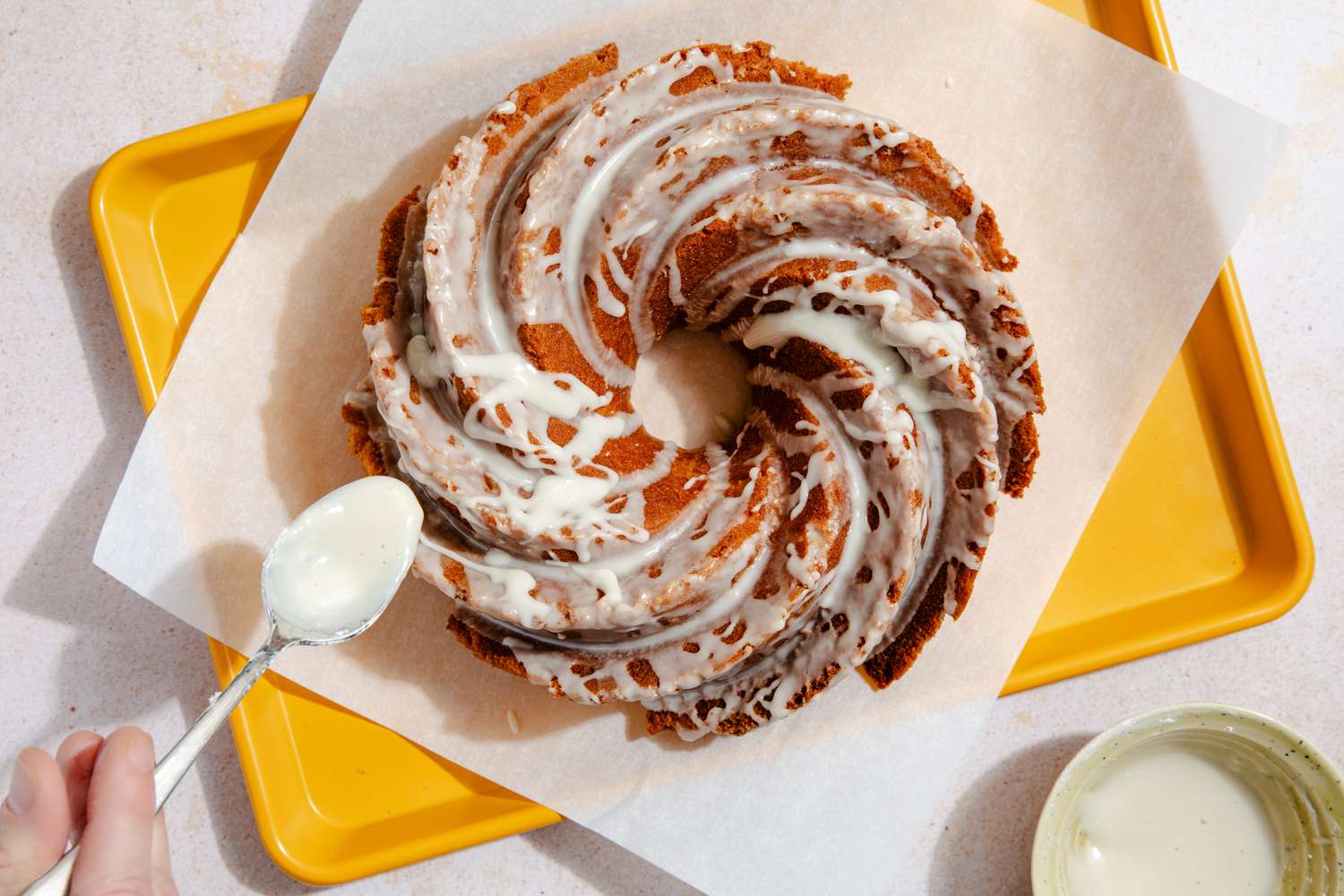 A top-down photo of a beautiful bundt cake with a hand spooning icing over the top