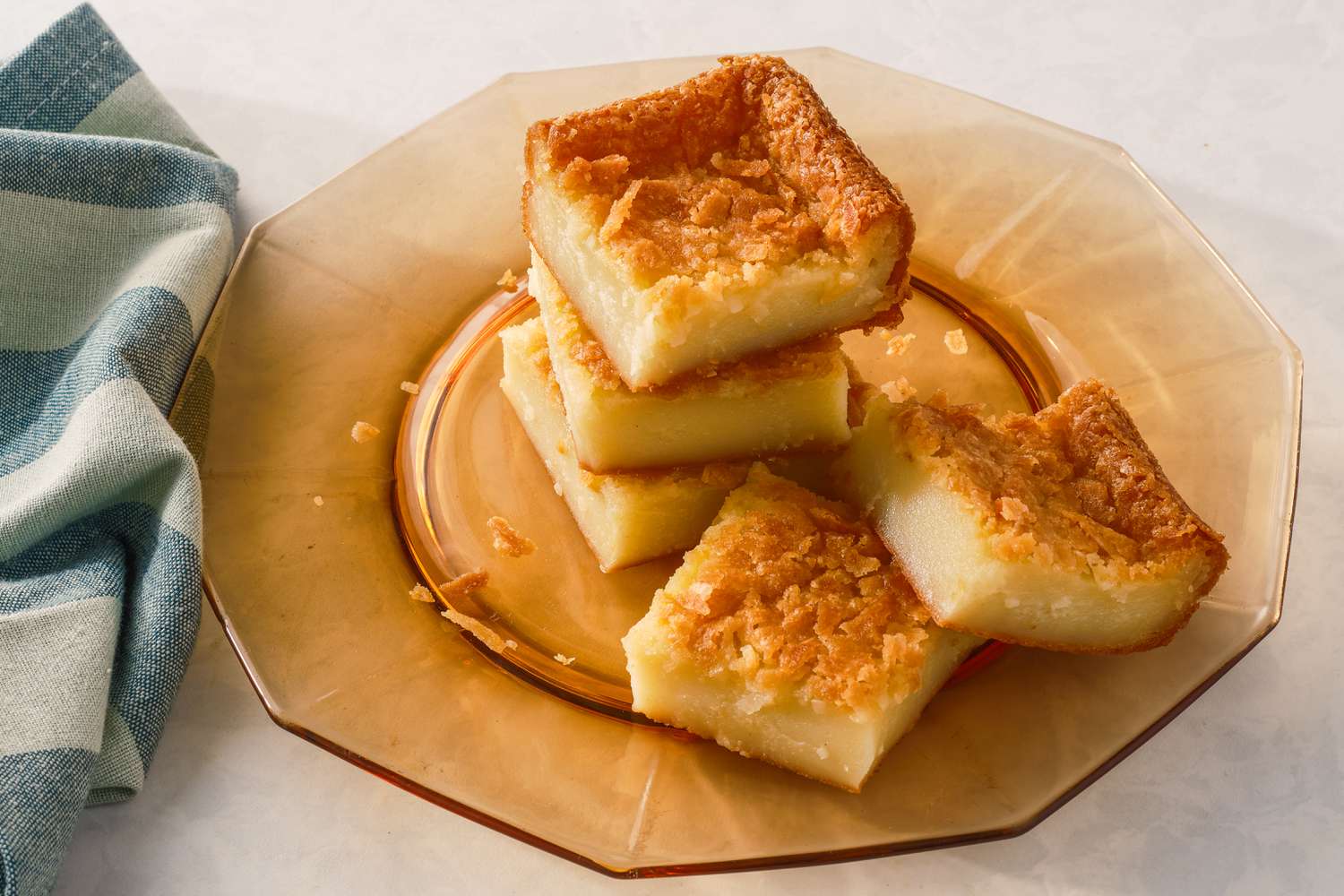 Squares of butter mochi stacked on a orange plate
