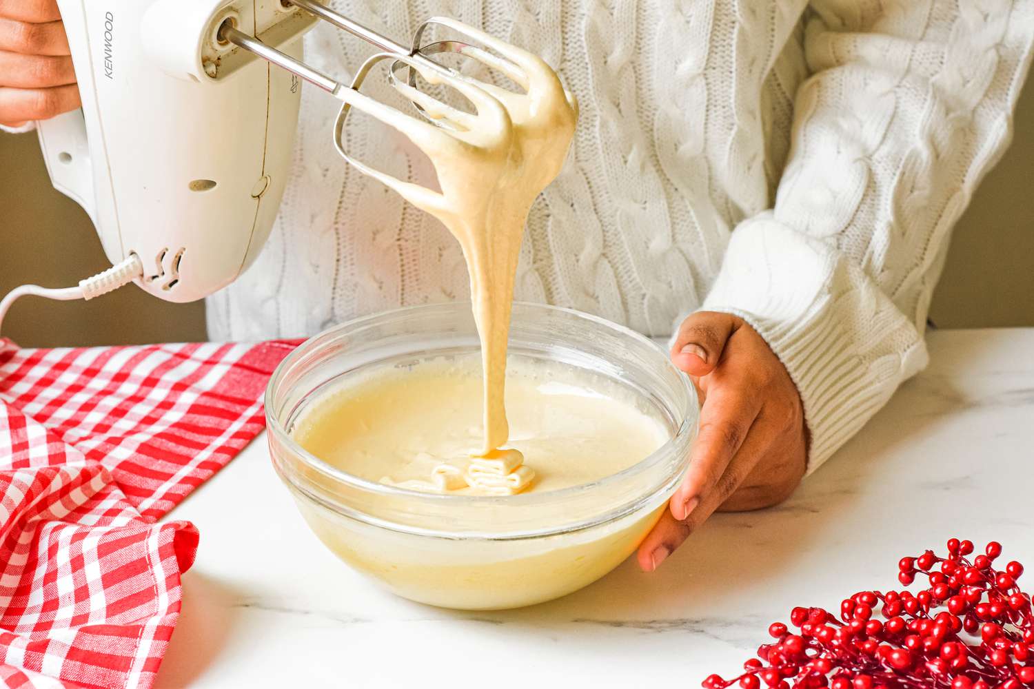 Eggnog mixture dripping from a hand mixer into a glass bowl.