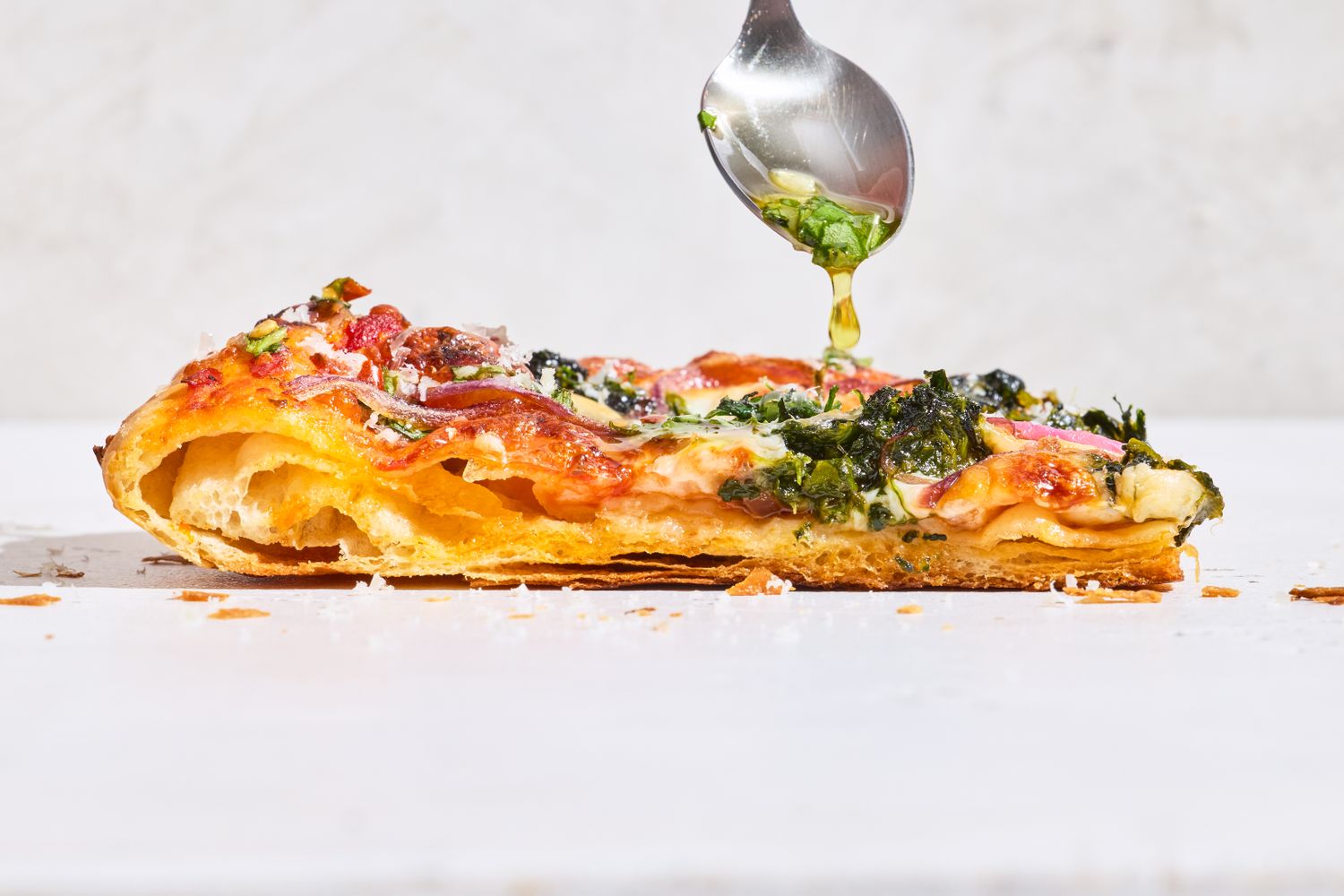 A slice of puff crust pizza being drizzled with herb sauce from a spoon