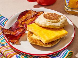An english muffin with a slice of baked egg, and two slices on bacon on the side