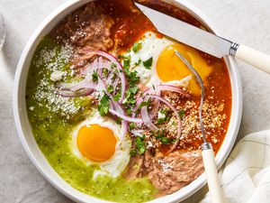 A white bowl with Huevos Divorciados, with a fork cutting into one of the egg yolks