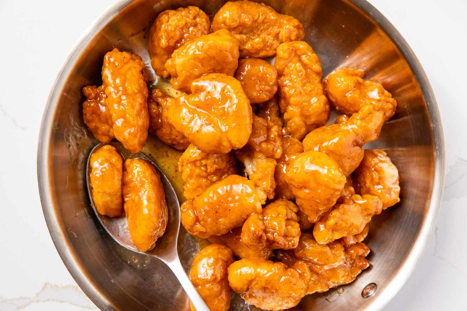 A pan of orange chicken with sauce and a spoon