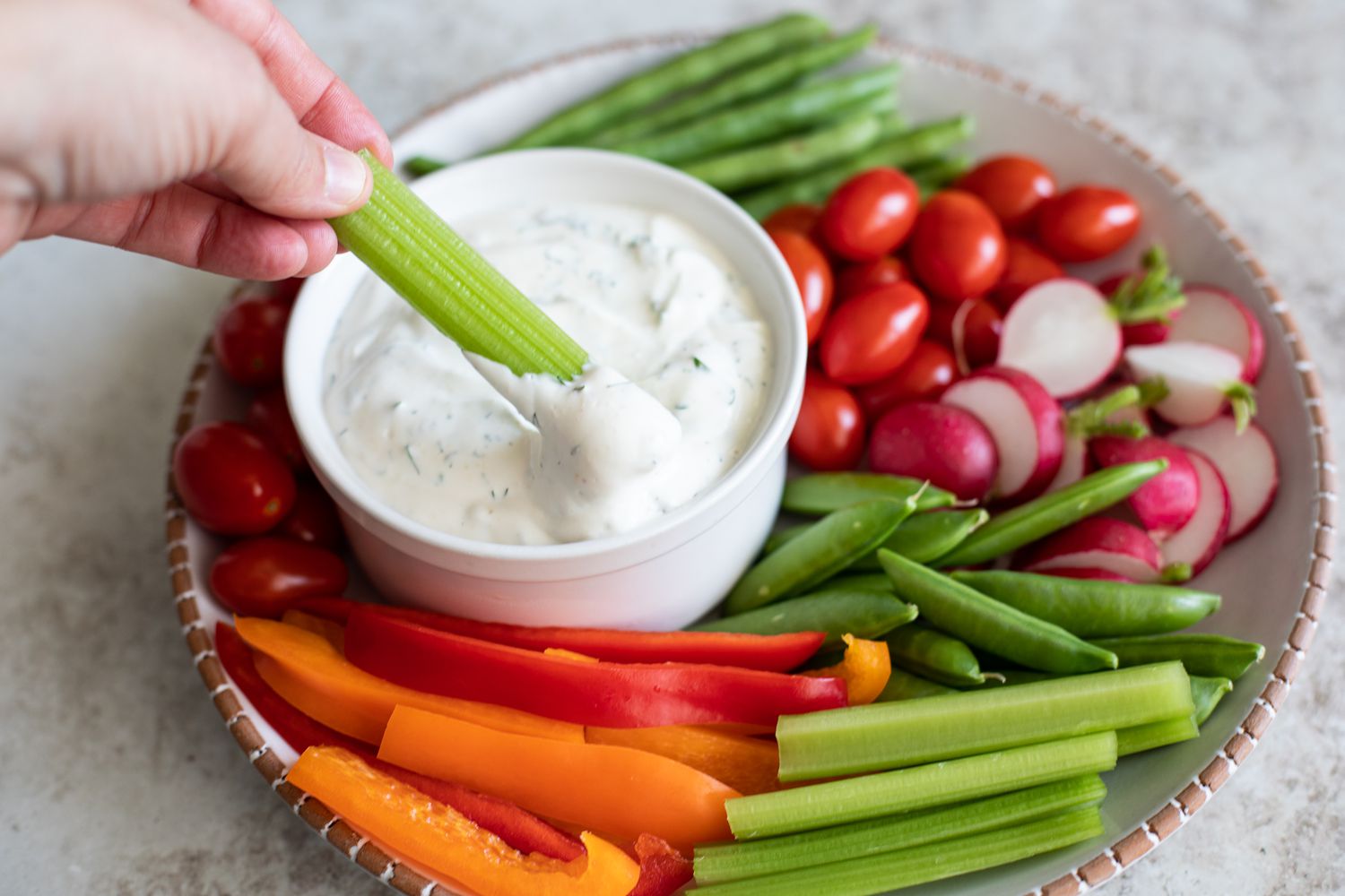 Platter of Vegetables and a Hand Dipping Celery in a Bowl of Veggie Dip