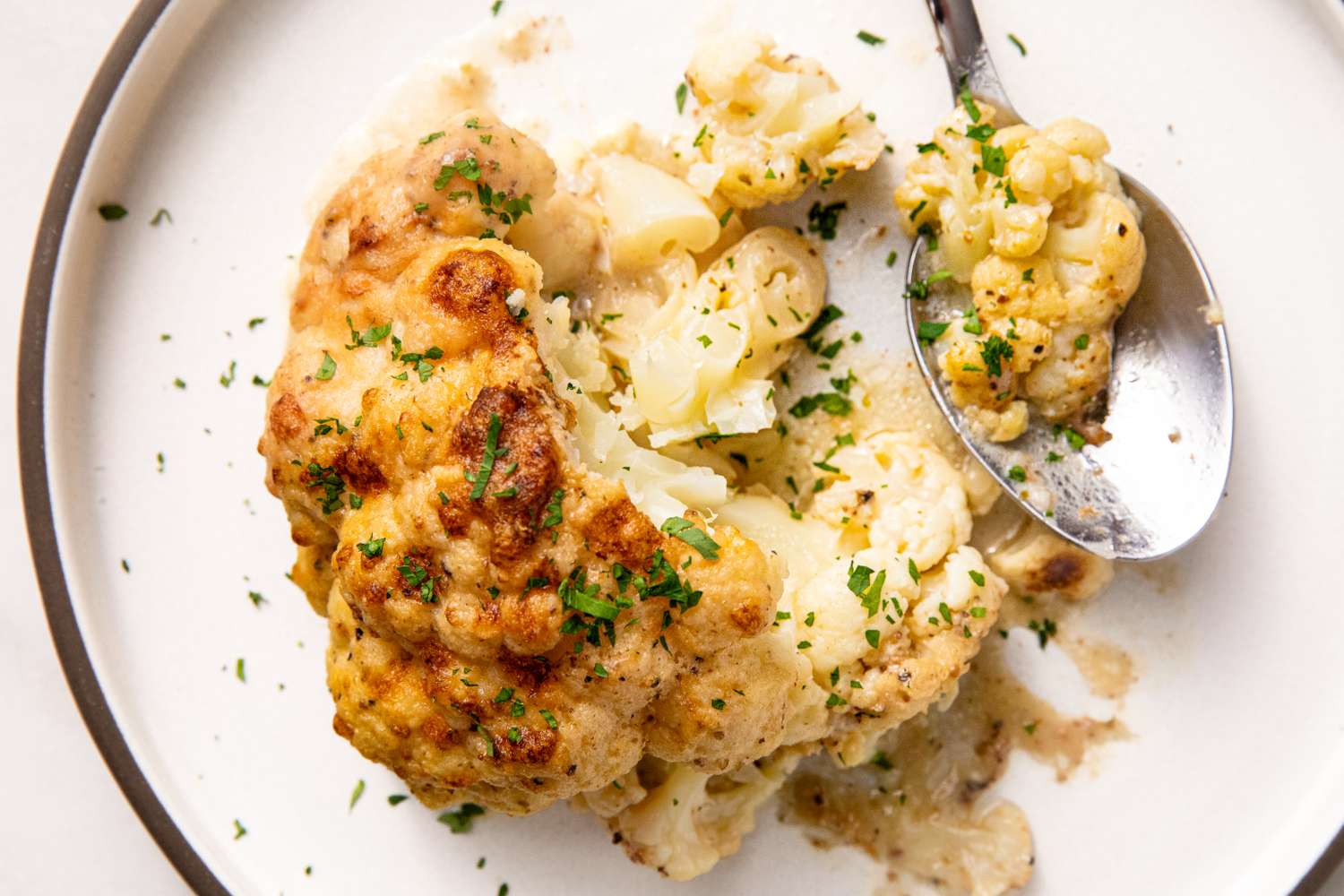 A closeup view of roasted cauliflower on a plate garnished with herbs with a spoon scooping a portion