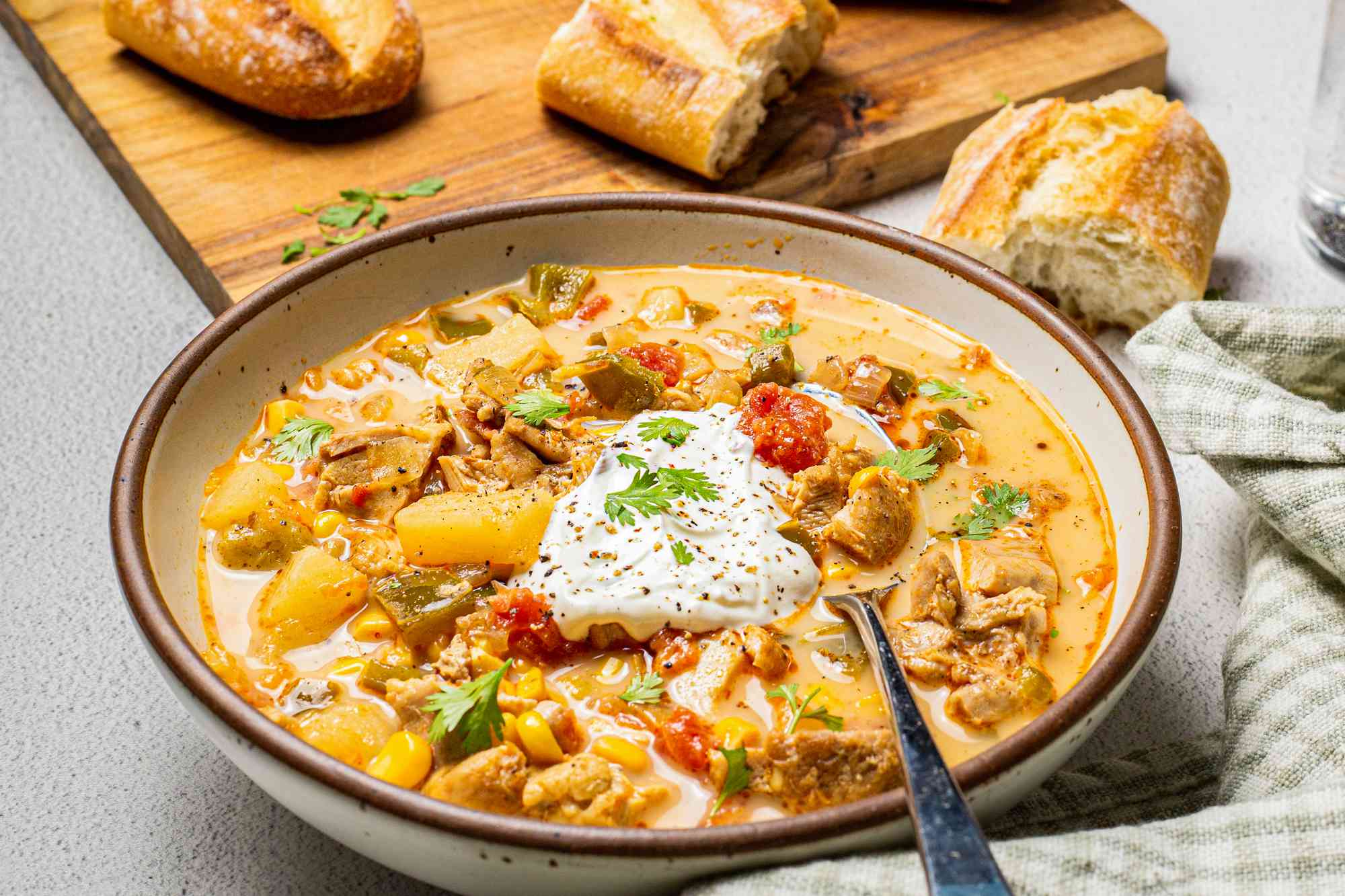 Bowl of Chipotle Chicken Chowder with a Wooden Board with Baguette Pieces in the Background