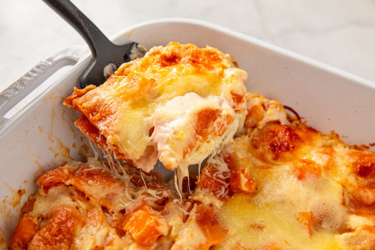 A serving of butternut squash ravioli lasagna being lifted from a baking dish with a spatula