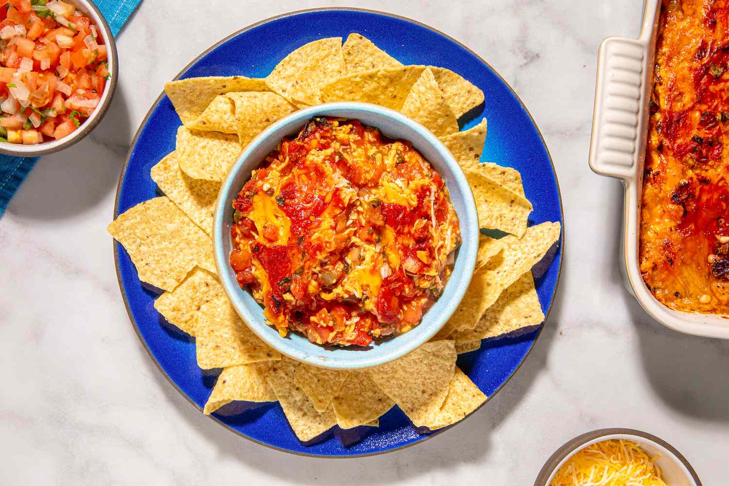 A bowl of tomato and cheese dip surrounded by tortilla chips on a blue plate