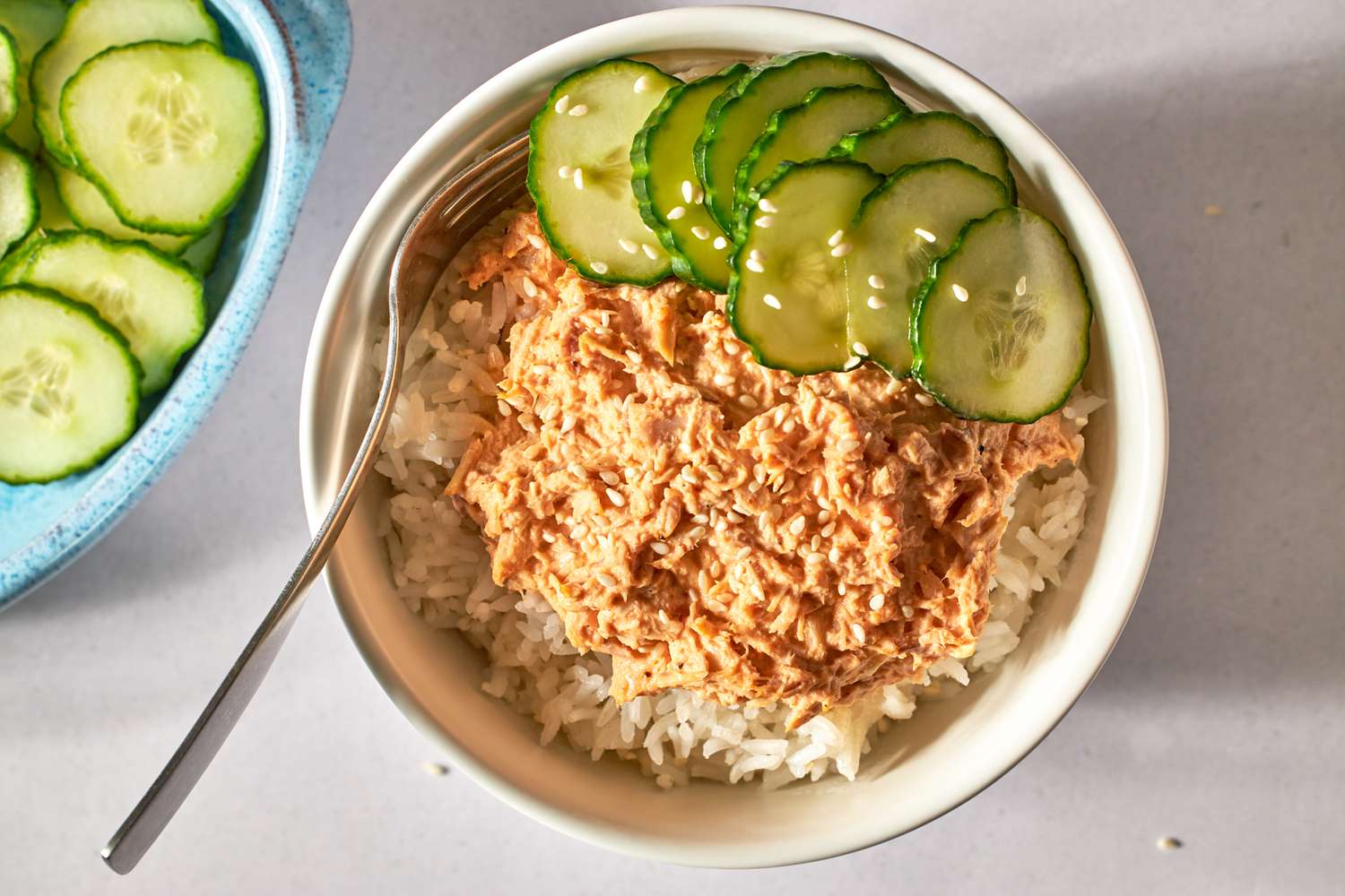 Rice bowl topped with spicy tuna and sliced cucumber, fork on the side.