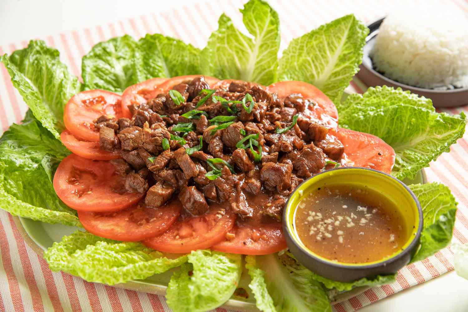 Lok Lak Served Over Sliced Tomatoes and Lettuce on a Platter With a Bowl of Pepper-Lime Sauce, and in the Background, a Bowl of Rice