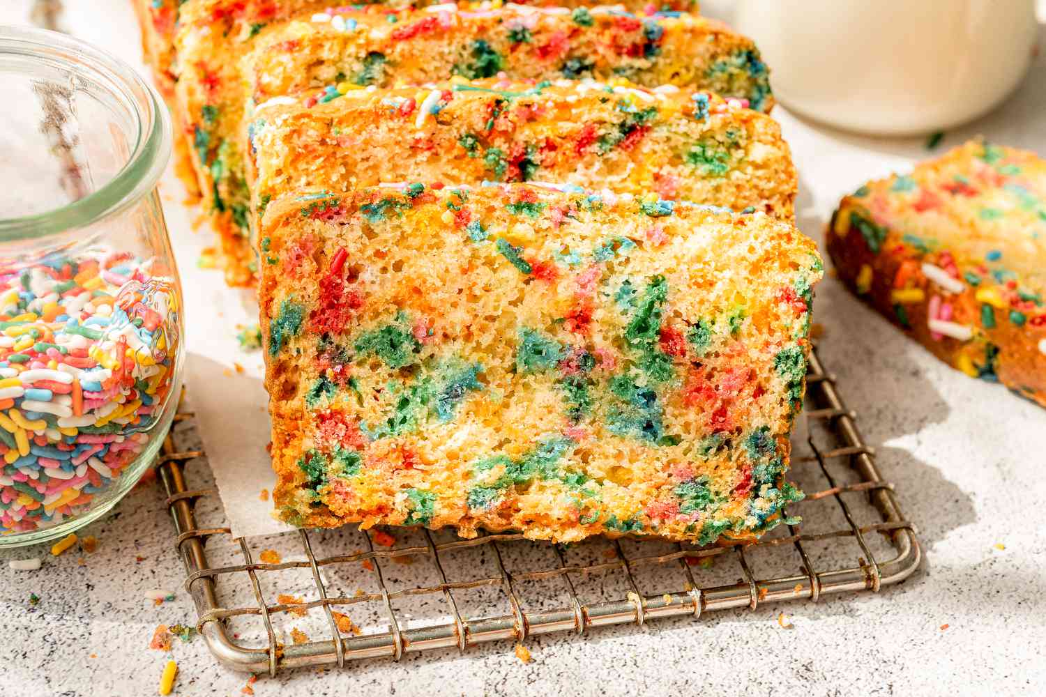 sliced ice cream bread on a wire rack, and in the surroundings, a jar of sprinkles and a jar of milk