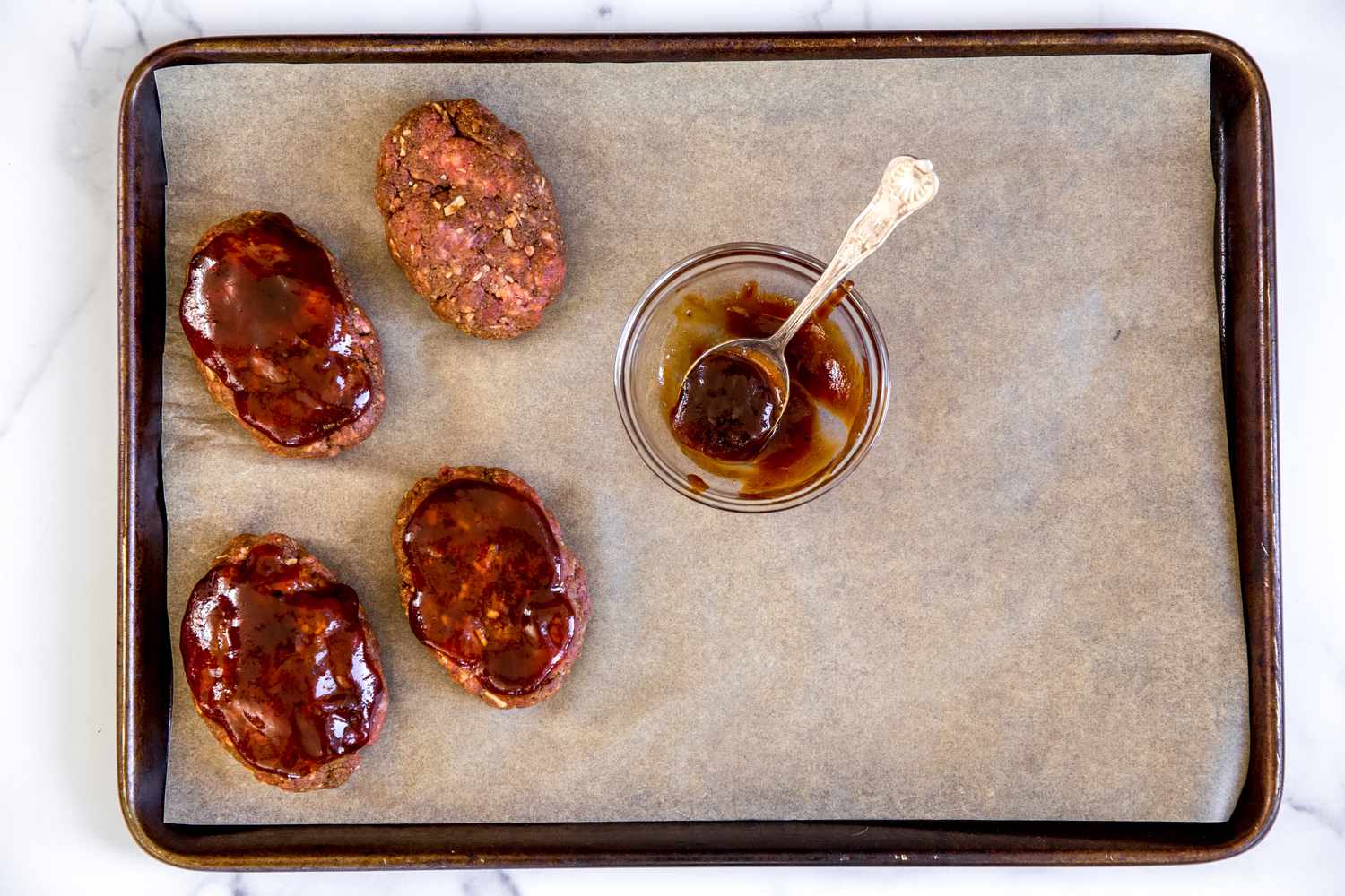 Glaze added to mini meatloaves on a sheet pan.