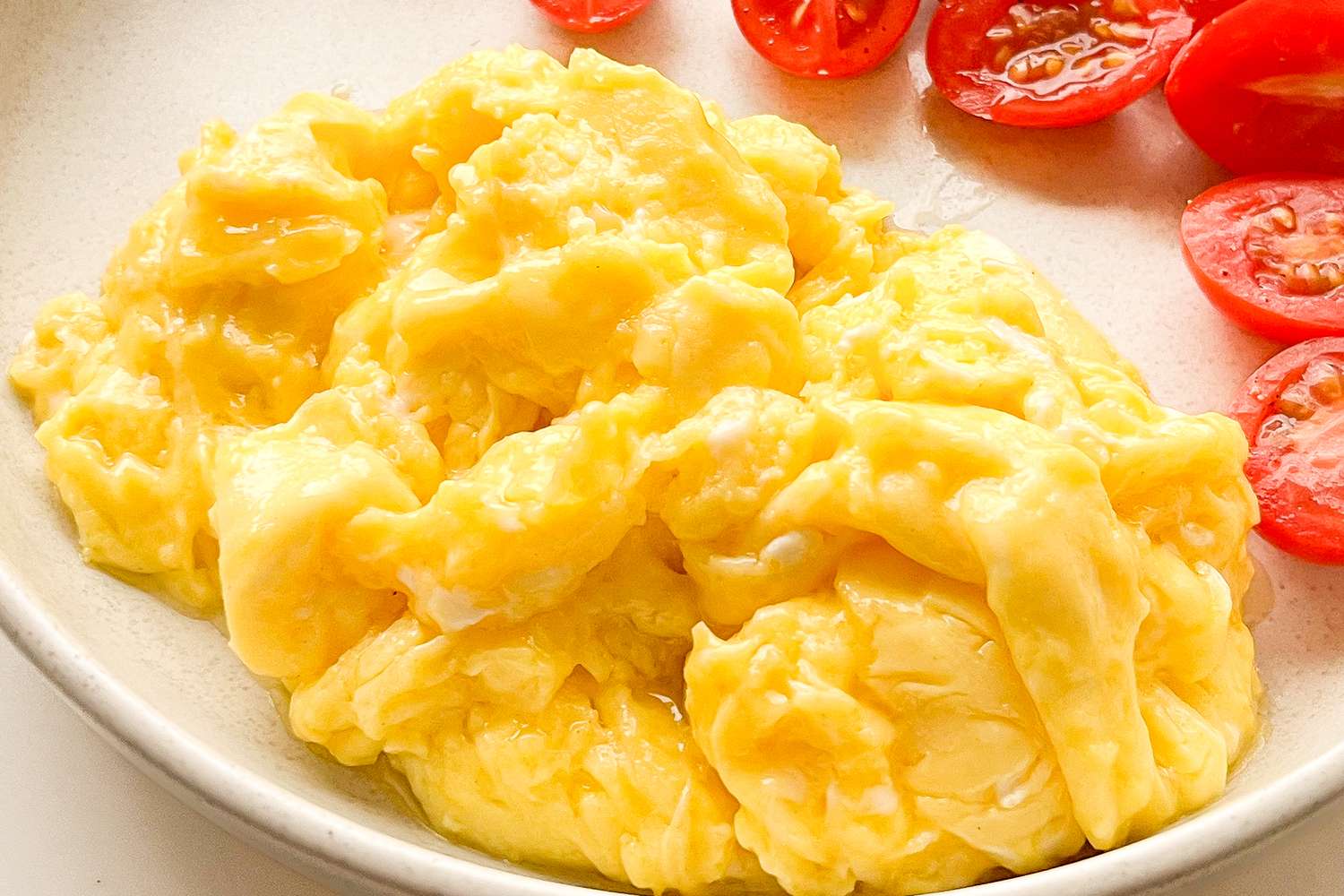 Scrambled eggs served on a plate with sliced cherry tomatoes