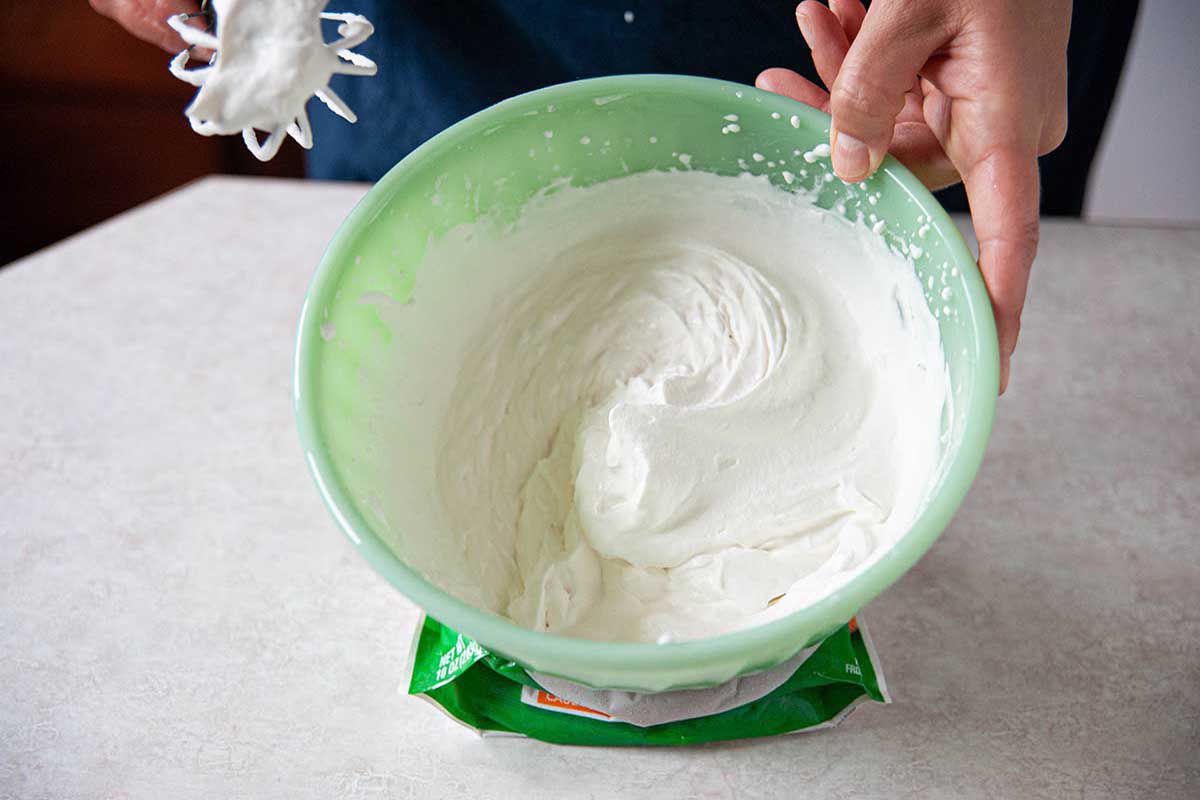 Homemade whipped cream in a mint green bowl set on a bag of vegetables.
