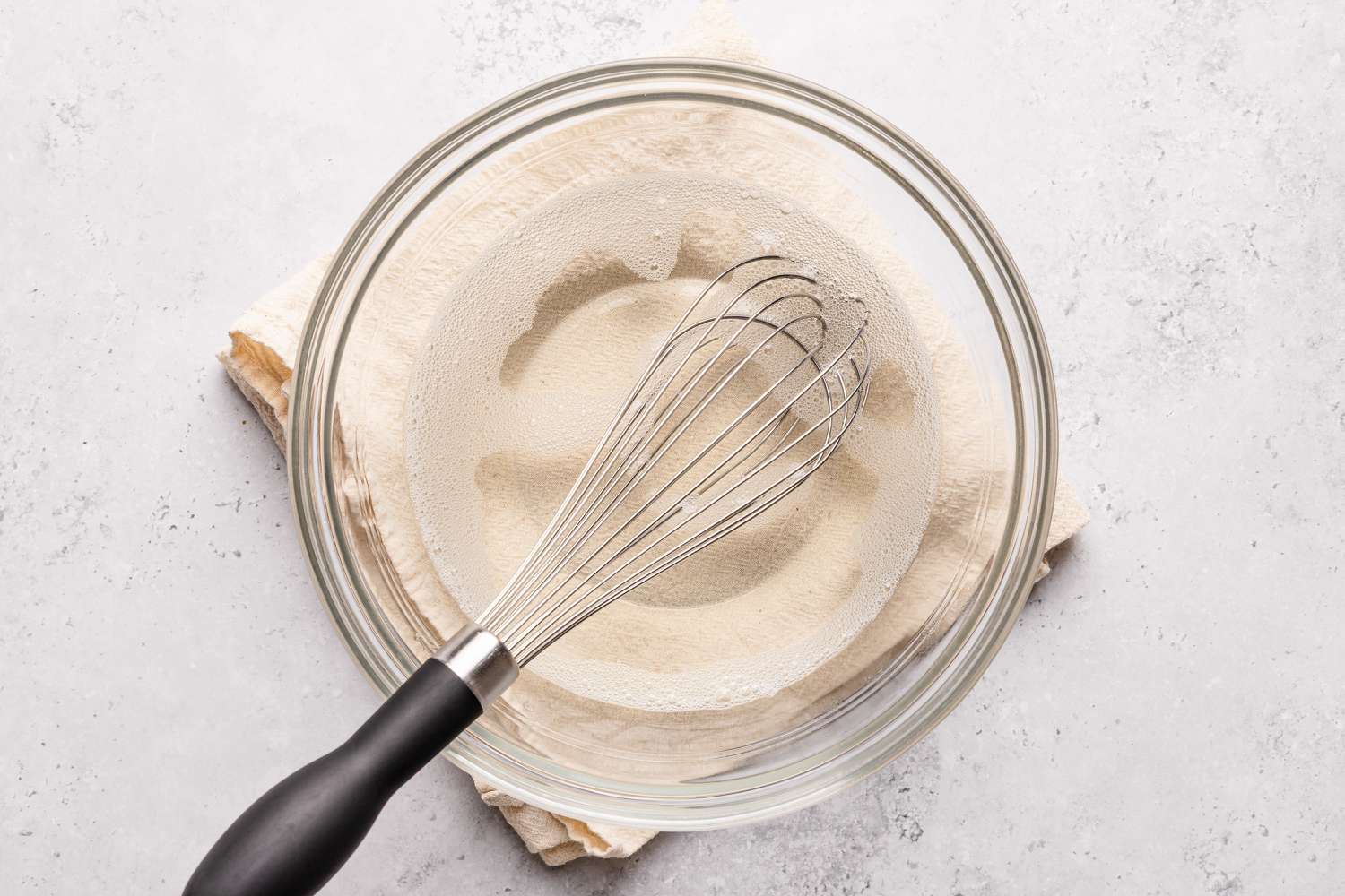 OVerhead shot of a whisk in a clear bowl with water and clear genlatin for the stained glass jello recipe