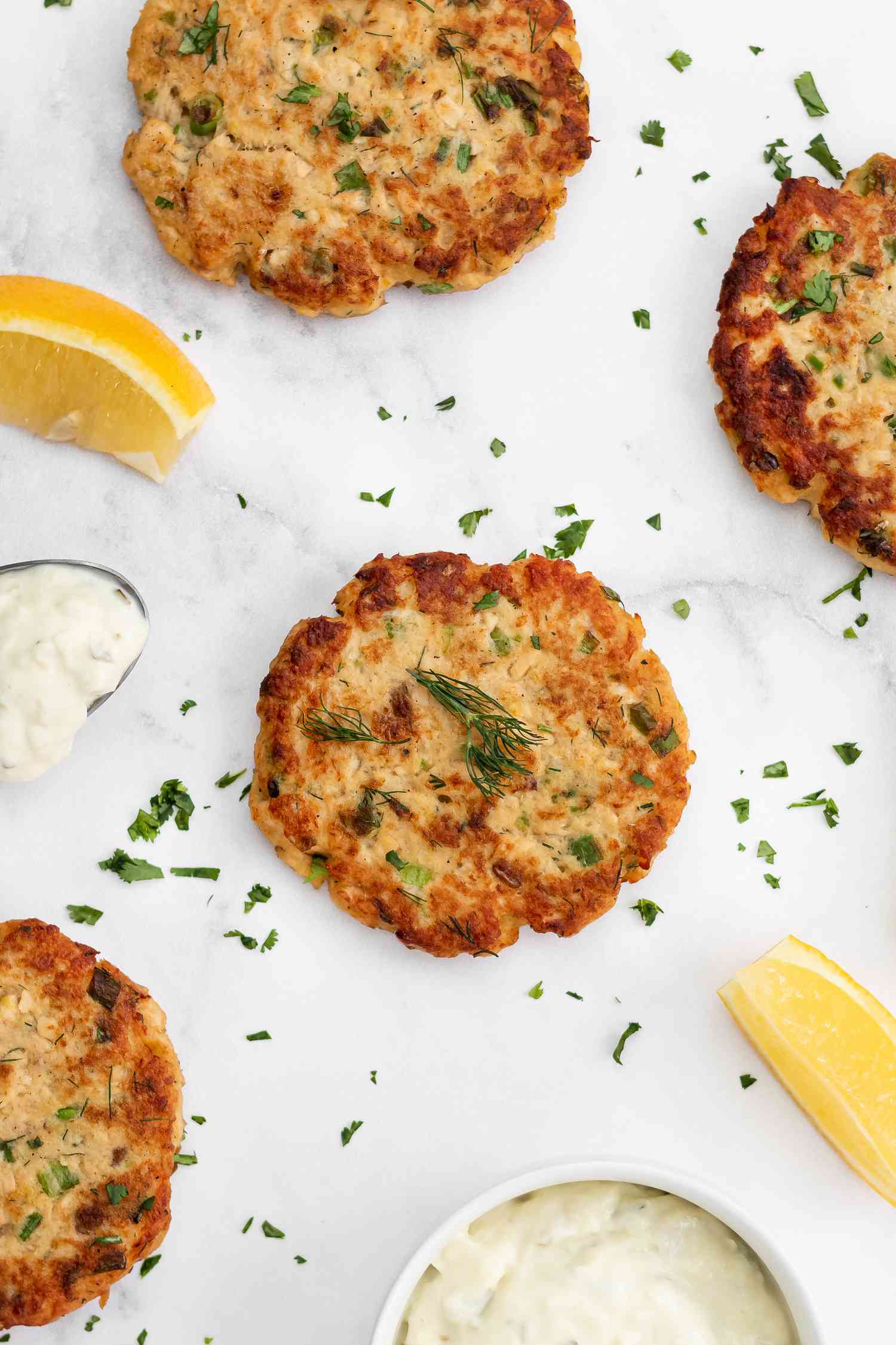 Salmon patties on a white background with a dip and lemon wedges.