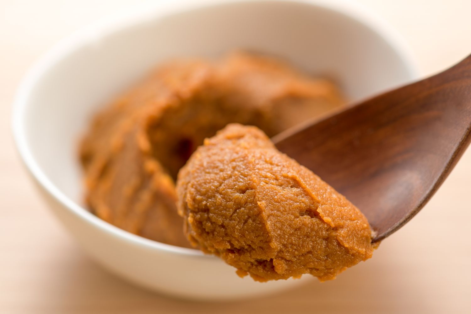 A wooden spoon holding a scoop of miso paste over a white bowl