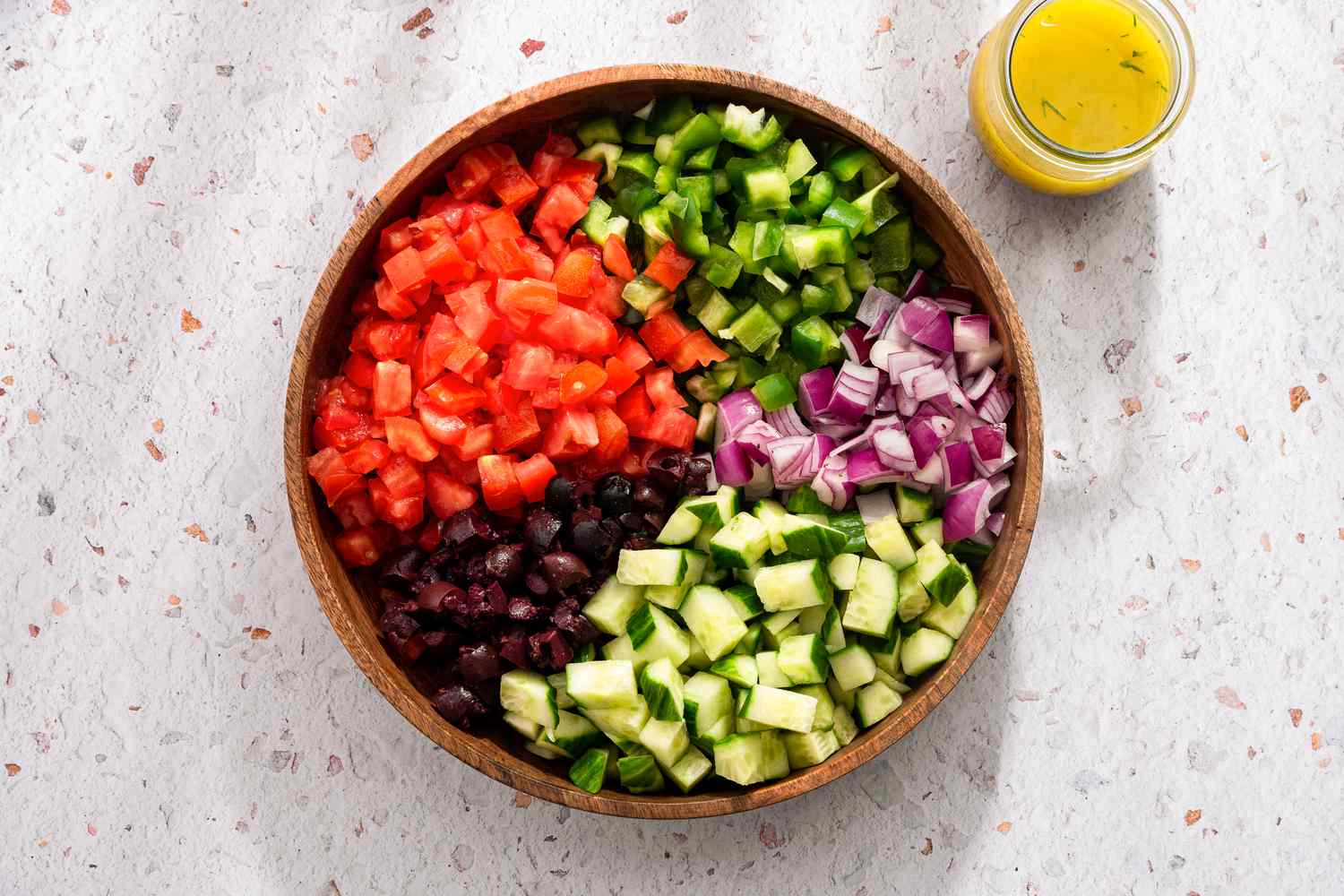 Greek Salad Ingredients in a Bowl in Separate Piles, and Next to the Bowl, a Jar of Greek Salad Dressing 