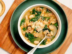 A white bowl with kale, white bean and sausage soup, places on a dark green plate on a wooden serving board