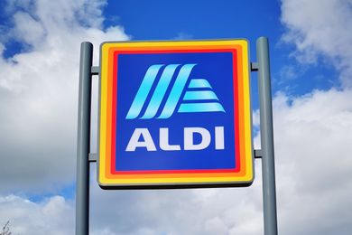 An Aldi supermarket sign mounted on poles against a cloudy sky
