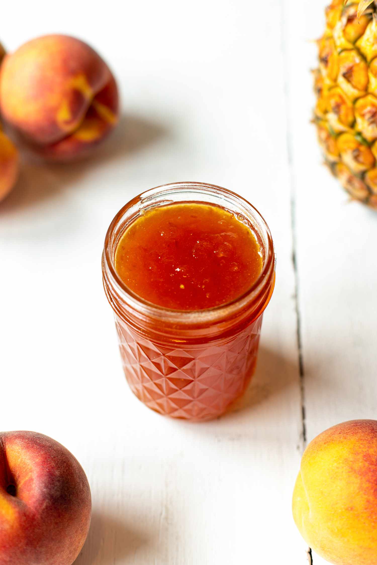Peach and Pineapple Jam Surrounded by Peaches and a Pineapple