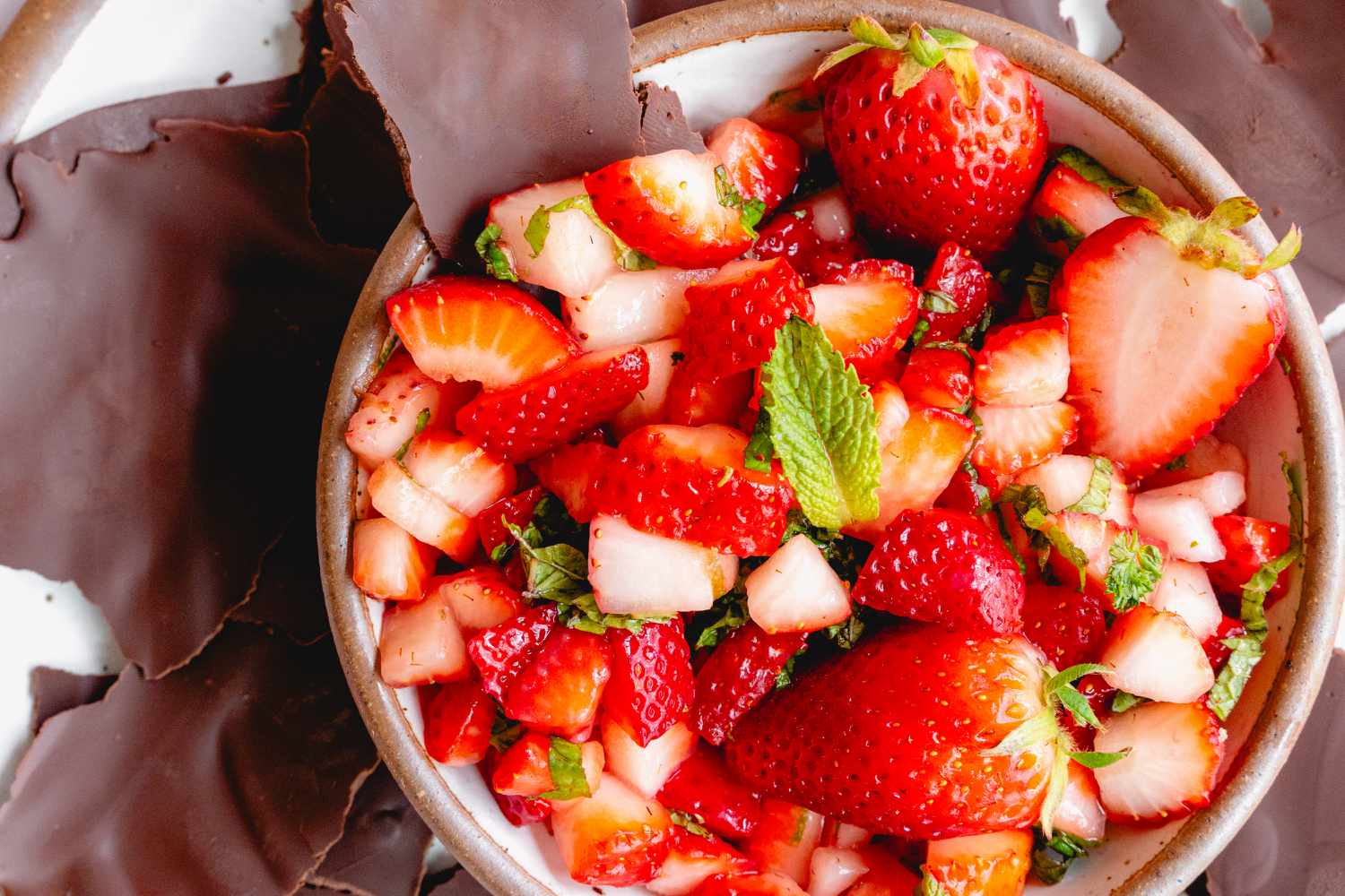 A bowl of strawberry salsa surrounded by chocolate pieces