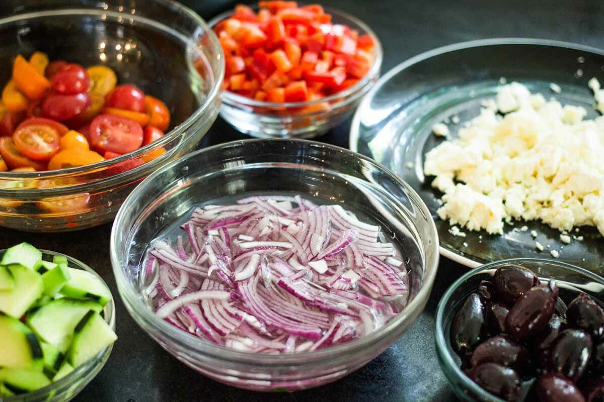 Ingredients in clear bowls for Greek pasta salad