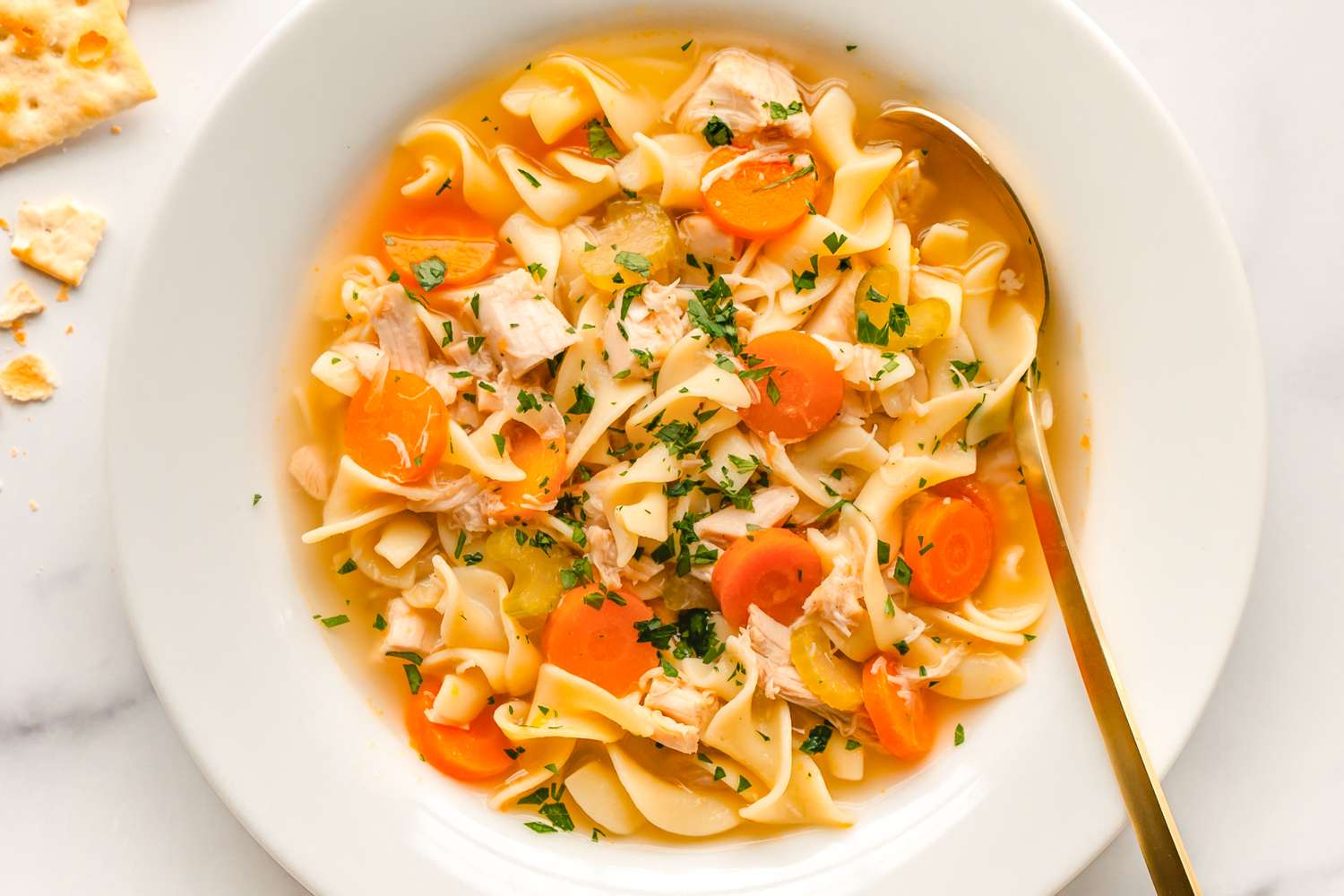 A bowl of chicken noodle soup with carrots noodles and herbs