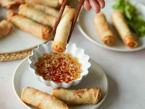 Dipping a spring roll into a sauce with more spring rolls on the plate and on a platter behind it.