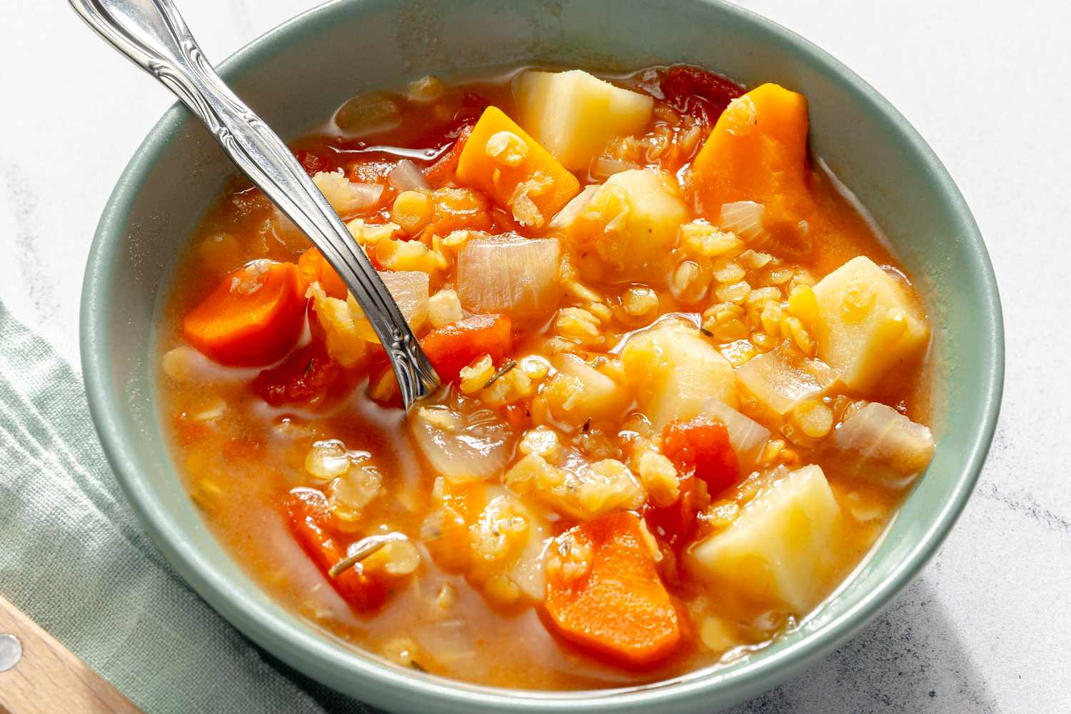 A bowl of red lentil soup with vegetables and a spoon