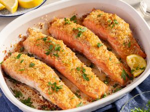 Angled view of a white baking dish of four salmon fillets topped with garlic butter, panko, and parmesan mixture and sprinkled with parsley