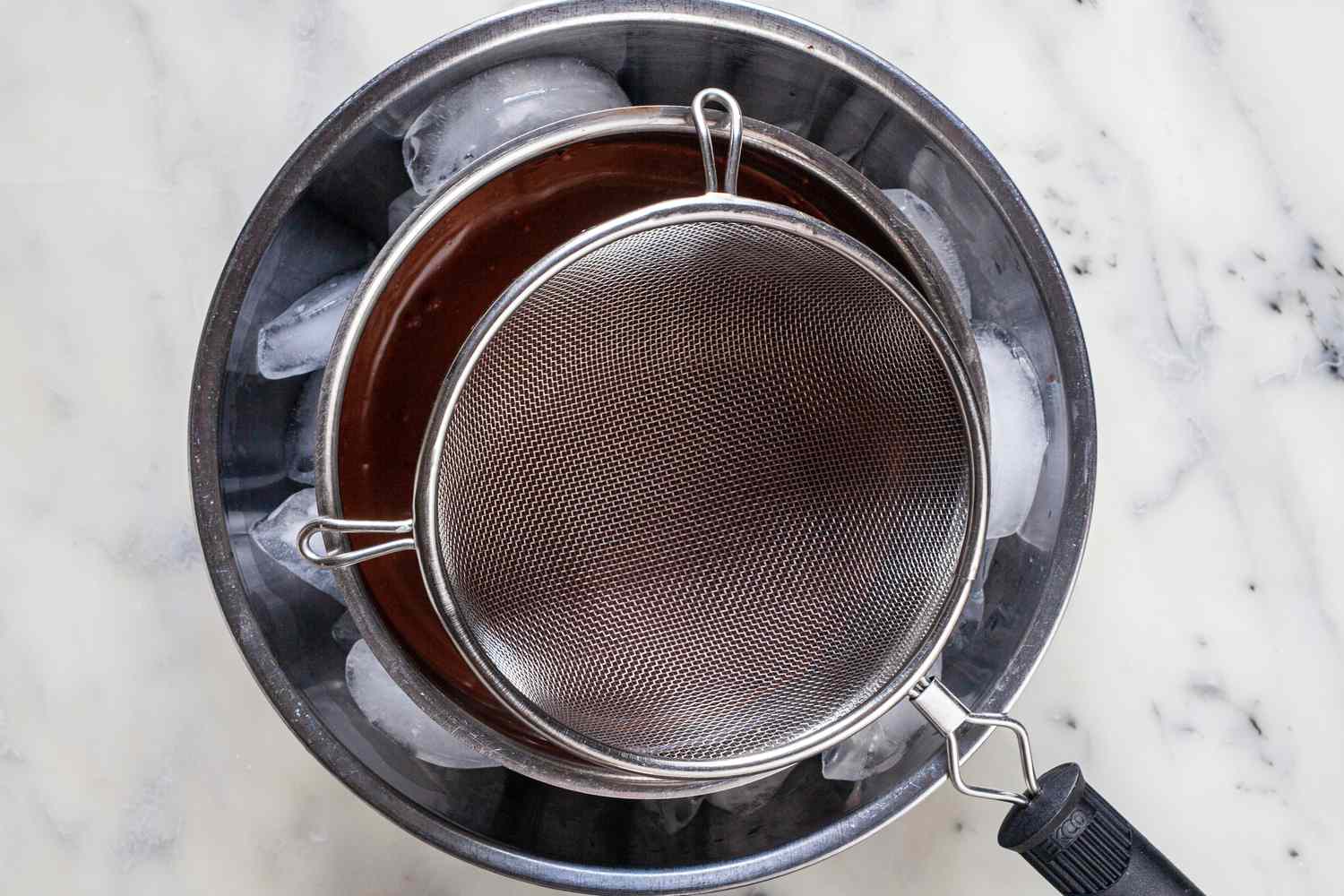 Strainer over chocolate in an ice bath to make mexican chocolate.