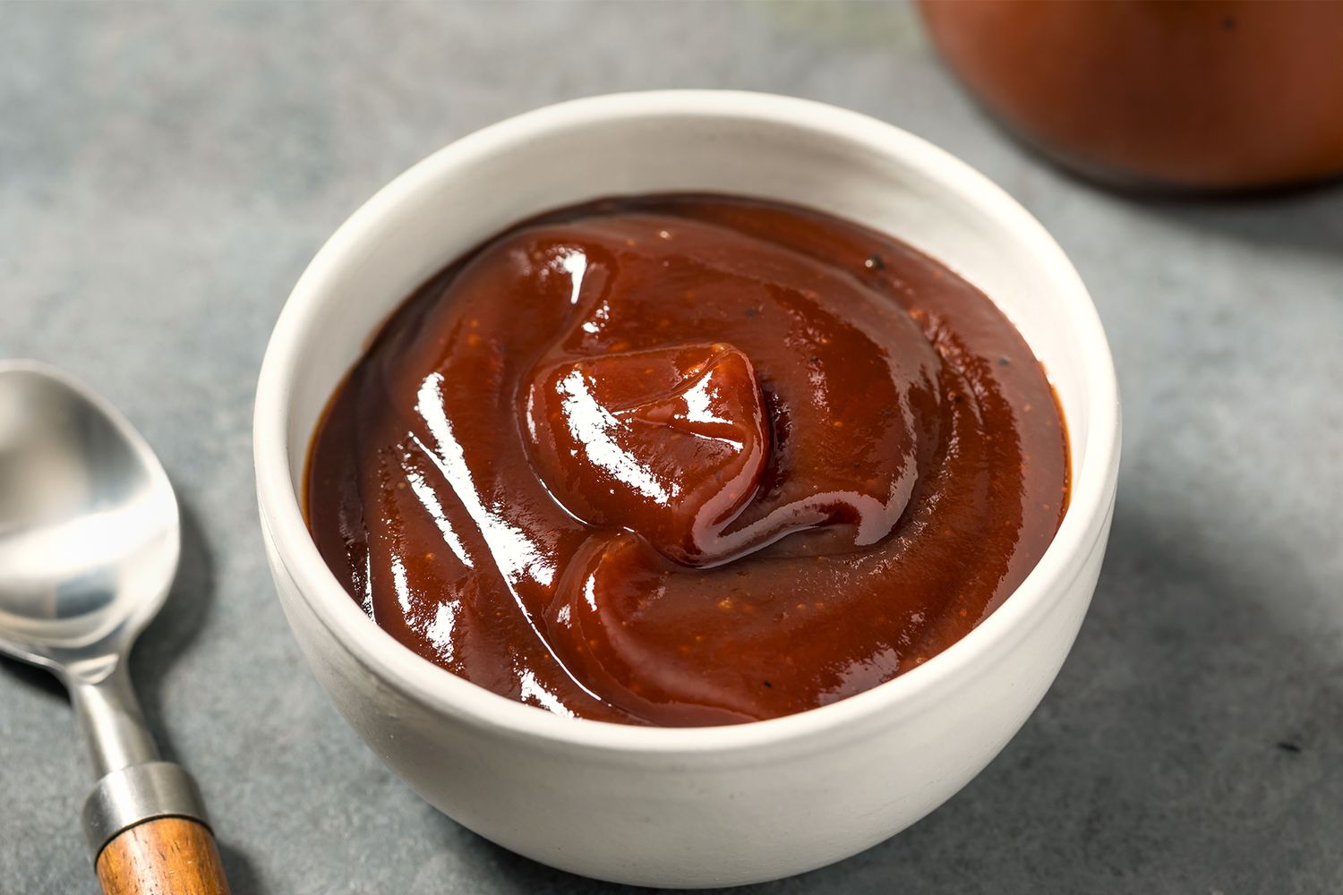 A bowl of thick barbecue sauce on a table with a spoon