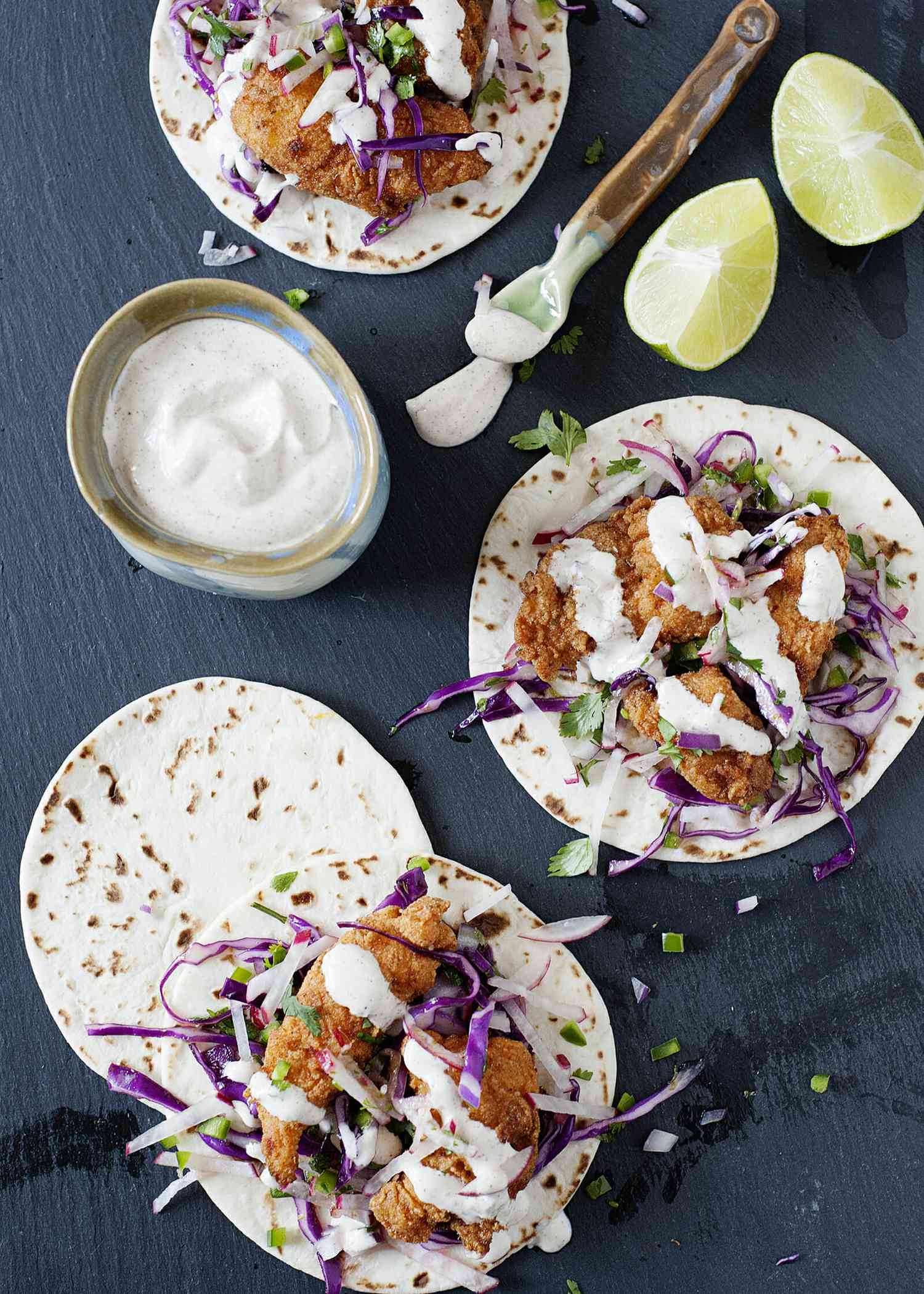 Crispy Fish Tacos with chili lime crema - fish tacos on grey slate with crema and lime