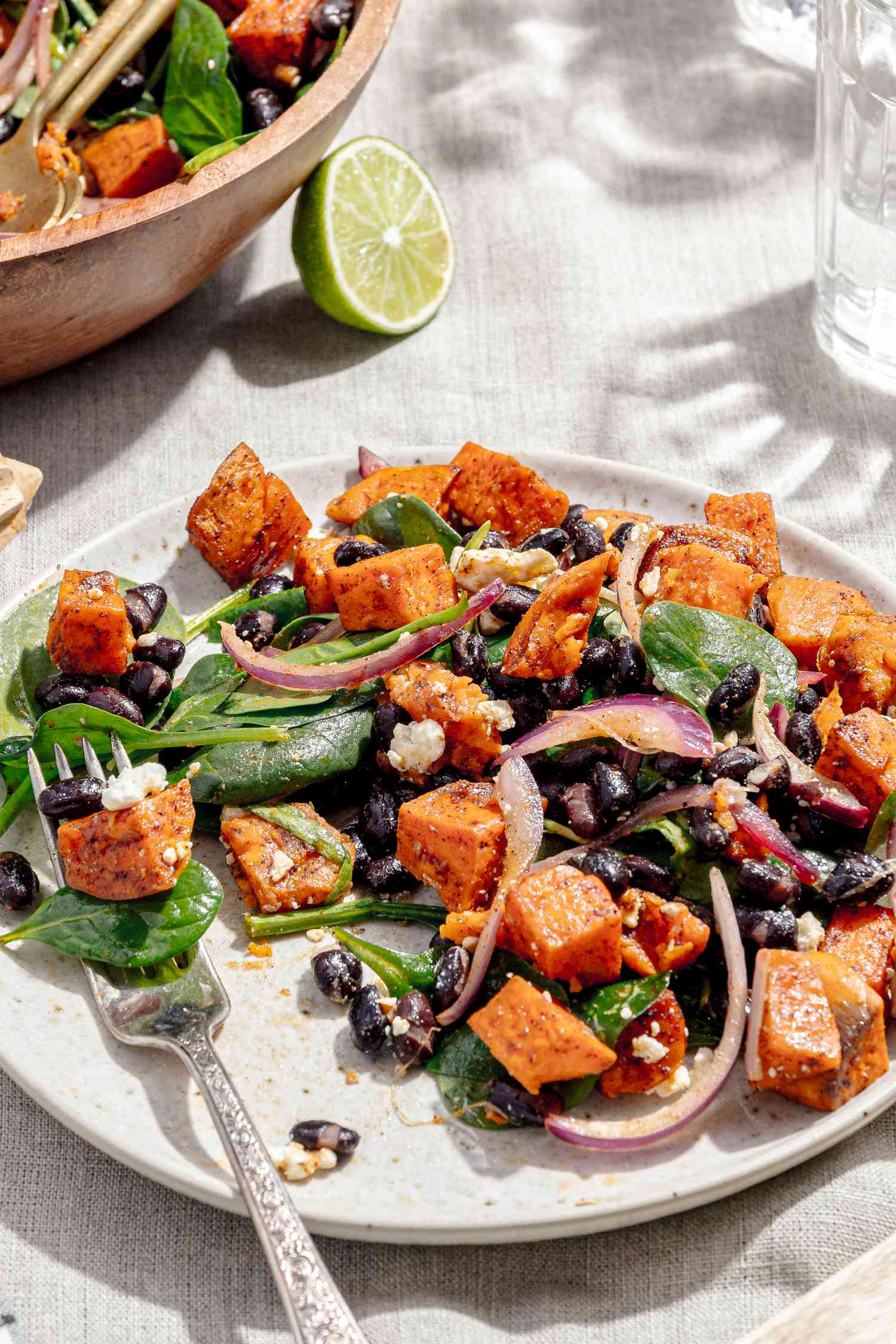 Plate of Roasted Sweet Potato Salad with a Fork, Surrounded by a Bowl with More Salad, Glasses, and a Small Bowl with Salt