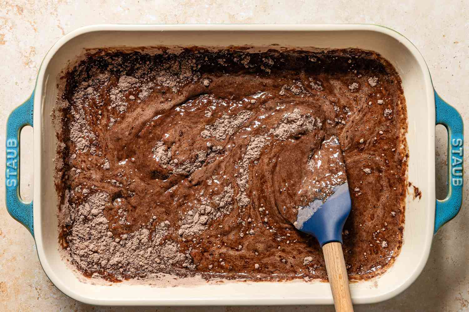 Overhead view of a baking dish after smoothing the cake and pudding mixes and chocolate chips for Chocolate Dump Cake recipe on a tan countertop