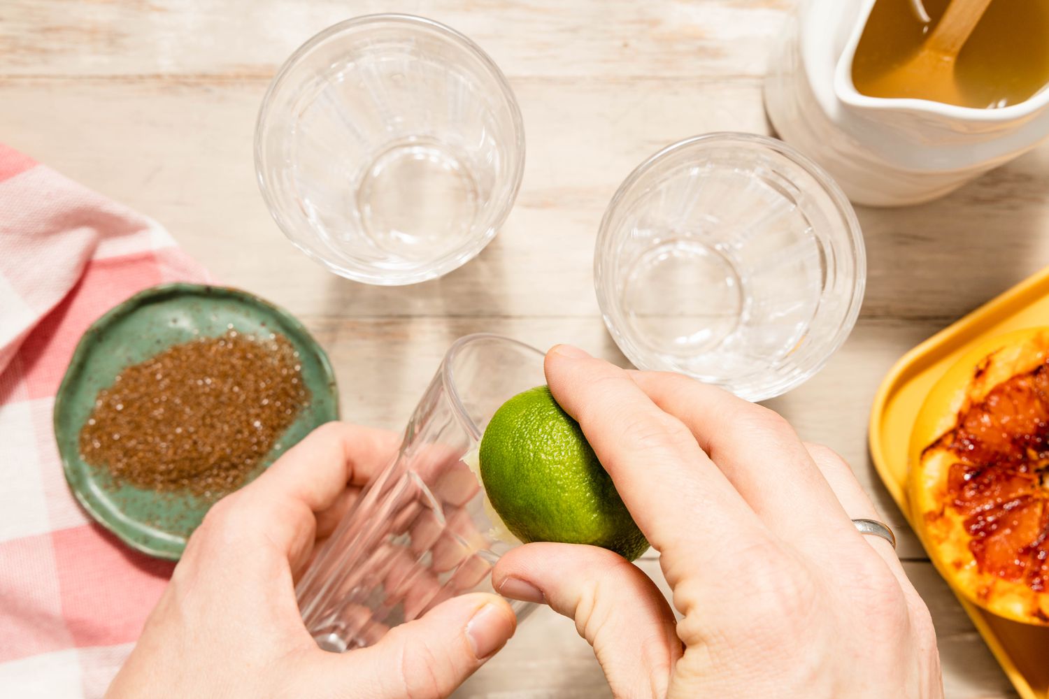 A Lime Half Rubbed Against a Glass Rim, and in the Surroundings, More Glasses, a Small Saucer of Smoked Salt, a Tray of Grilled Grapefruit, and a Pitcher With Lime-Vodka-Agave Mixture