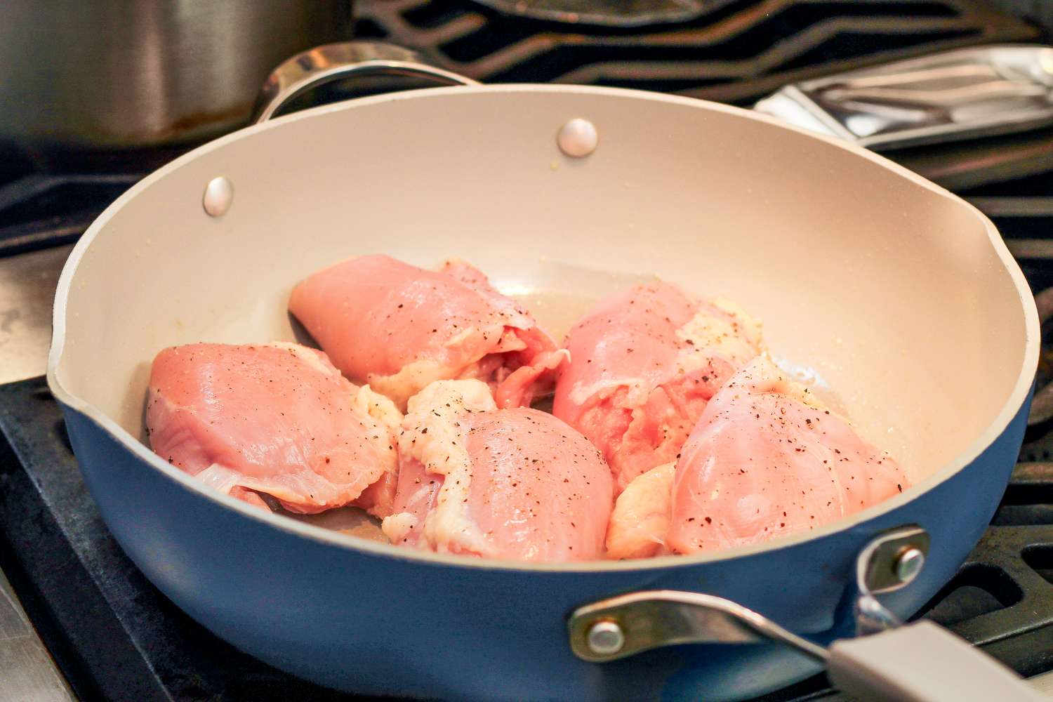 Chicken thighs cooking in a frying pan on a stove