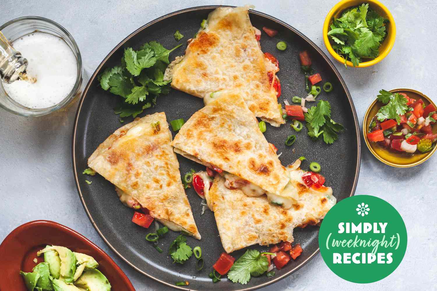 Wedges of quesadilla on a grey plate with cilantro, salsa, and avocado on the side