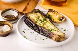 Plate of Whole Grilled Eggplant Next to a Platter of More Eggplant and an Oil Dispenser